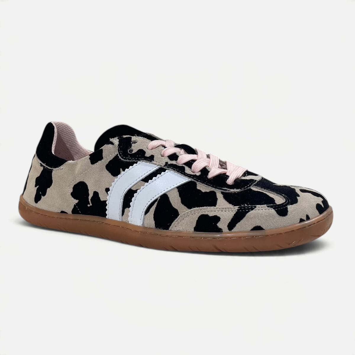 Zapatillas barefoot zoireo Coqueflex Trac con estampado de vaca, bandas blancas, cordones rosas y suela color caramelo.