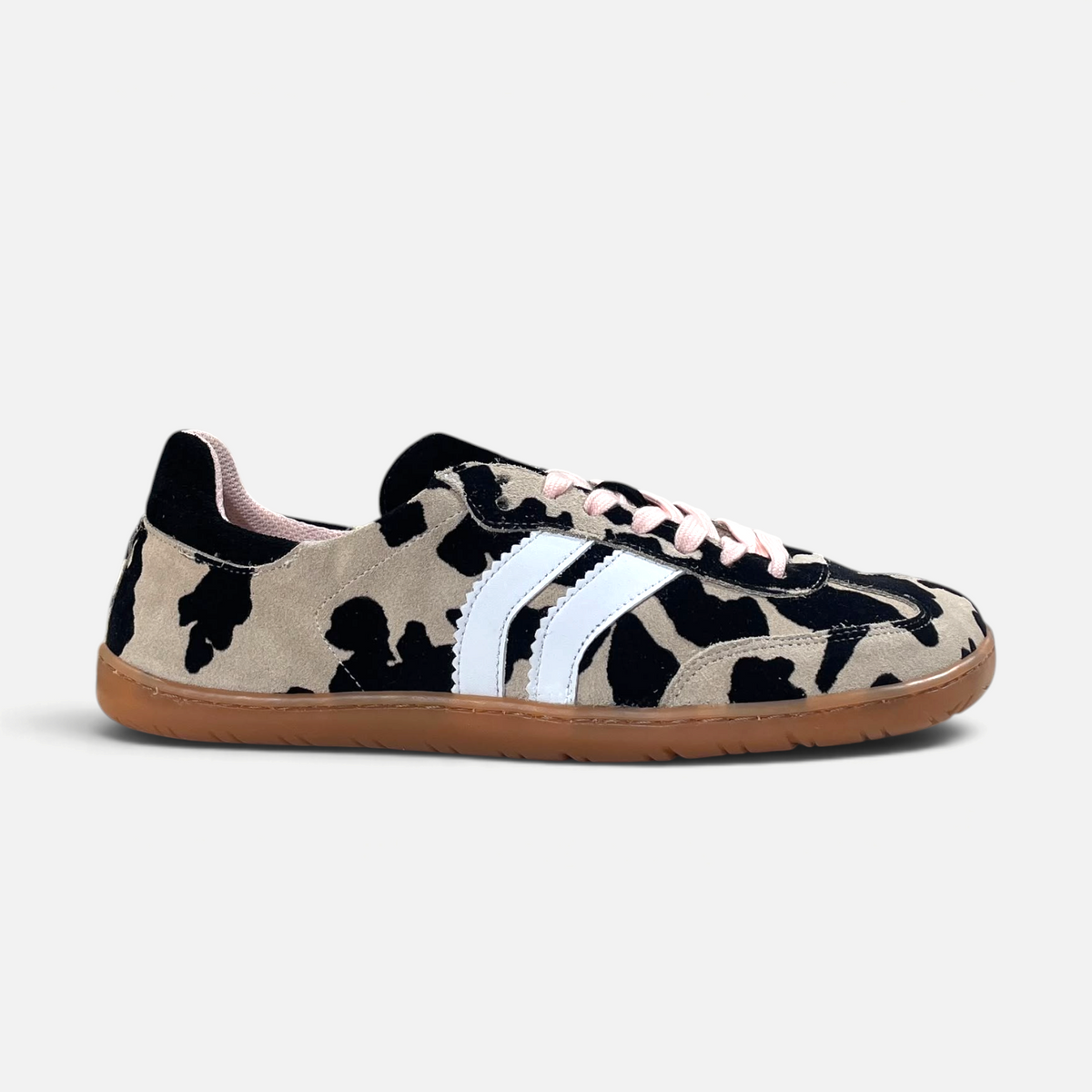 Zapatillas barefoot zoireo Coqueflex Trac con estampado de vaca, bandas blancas, cordones rosas y suela color caramelo.